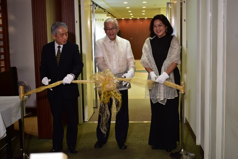 Photograph of two men and a women cutting a yellow ribbon with scissors