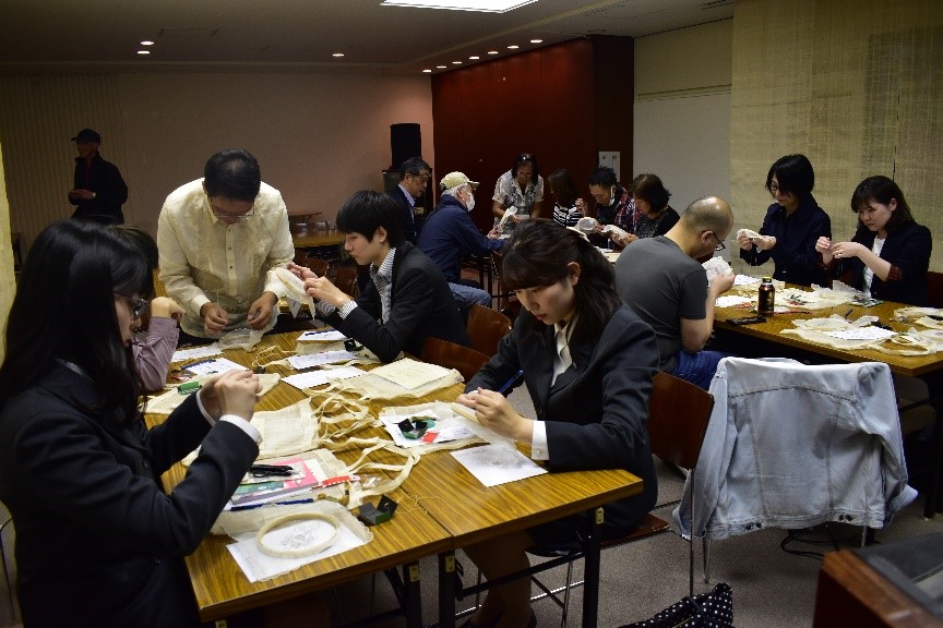 Photograph of people sat at tables taking part in an embroidery workshop