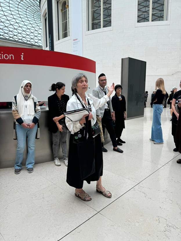 Photograph of a woman stood speaking to a group in the Great Court at the British Museum.