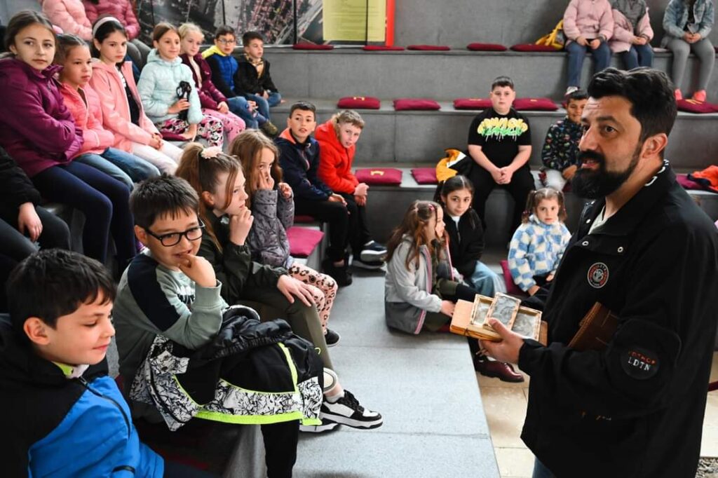 Photograph of a man speaking to a group of children.