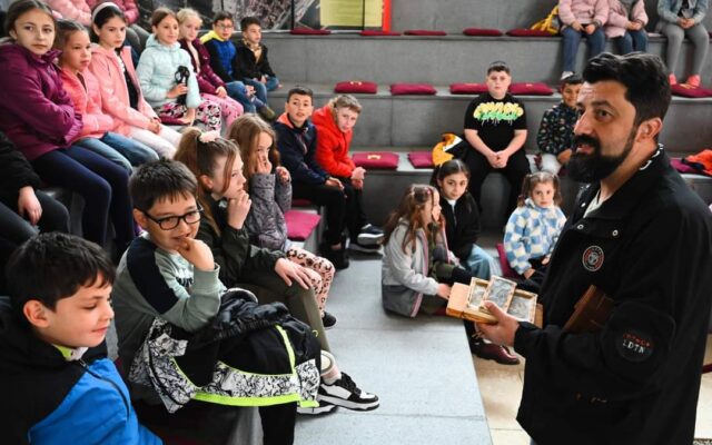 Photograph of a man speaking to a group of children.