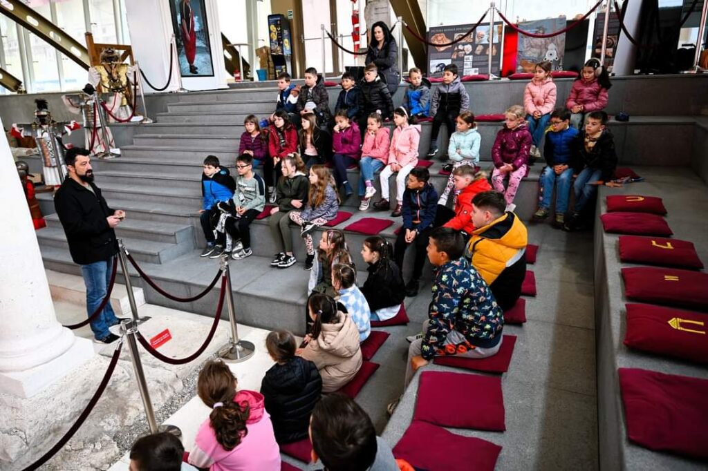 Photograph of children sat listening to a man talk.