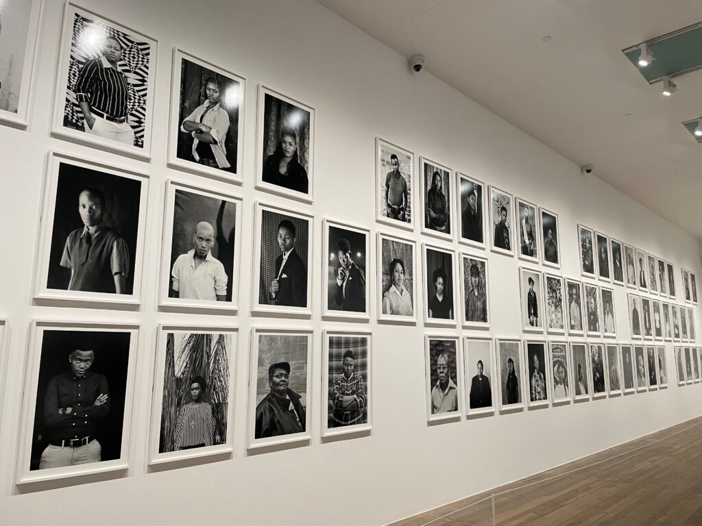 Photograph of a series of black and white portraits on a white wall.