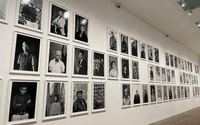 Photograph of a series of black and white portraits on a white wall.