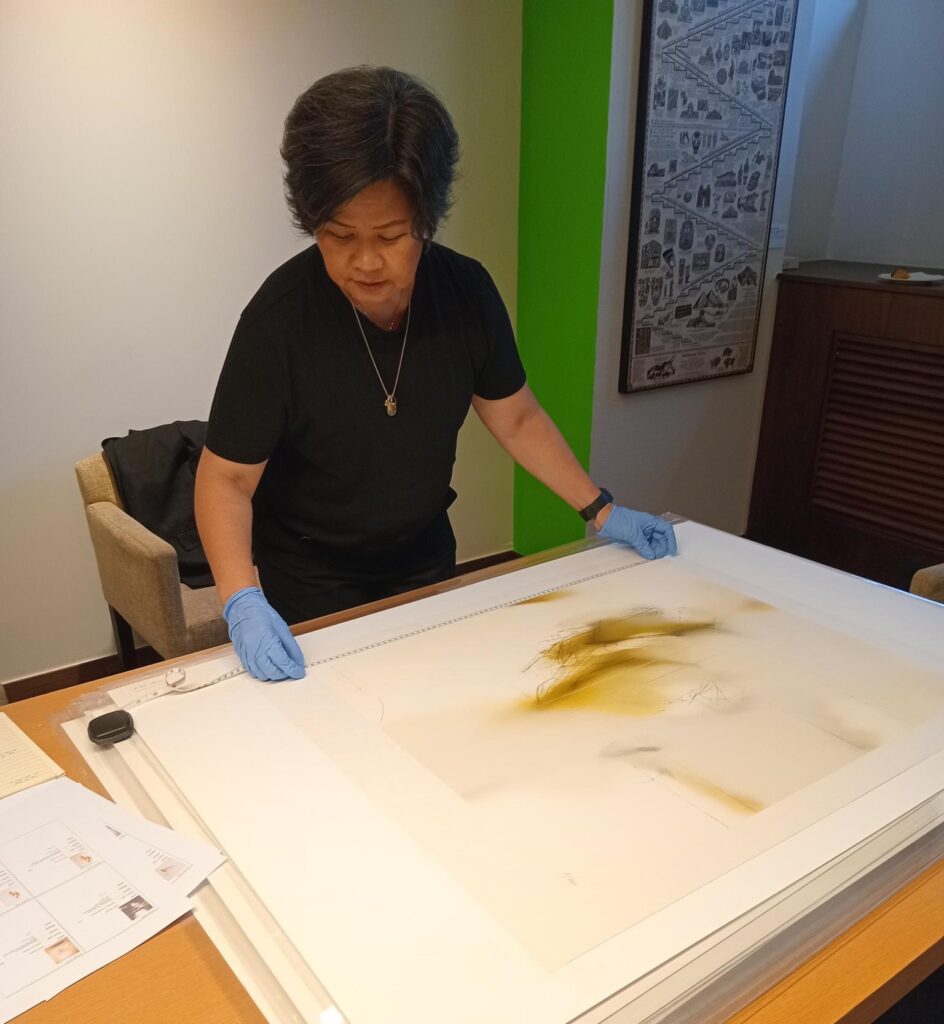 Photograph of a woman looking at a print on a table.