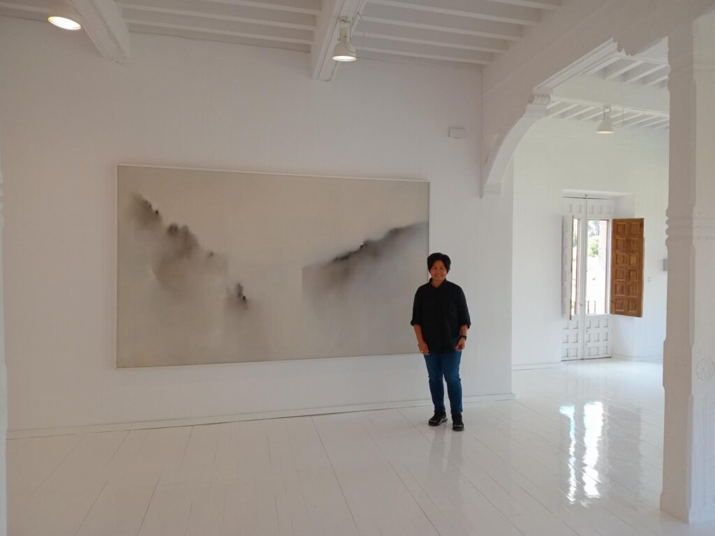 Photograph of a woman stood next to a print in a white gallery space.