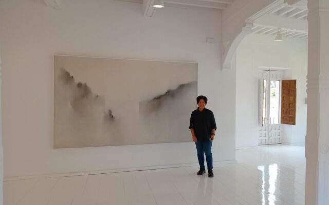 Photograph of a woman stood next to a print in a white gallery space.