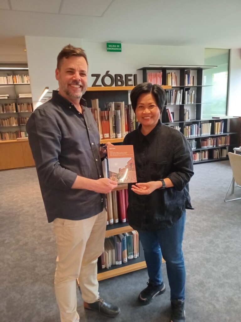 Photograph of a man and a woman stood holding a book and smiling,