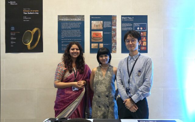 Photograph of three people stood in front of a poster.