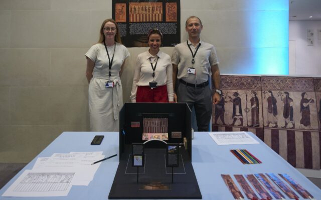 Photograph of three people stood behind a table with a display.